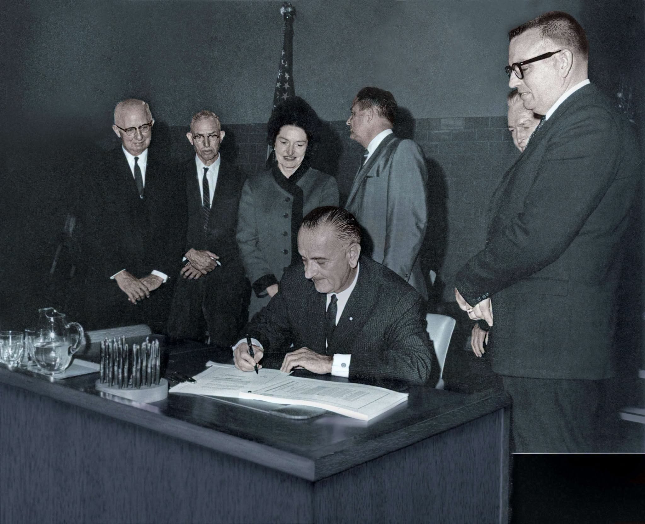 Tổng thống Lyndon B. Johnson ngồi ký Đạo luật Giáo dục Đại học năm 1965, xung quanh là các quan chức dự lễ