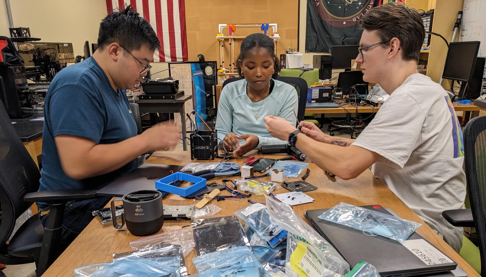 Ba sinh viên lắp ráp linh kiện vệ tinh quanh bàn trong TXST Space Lab